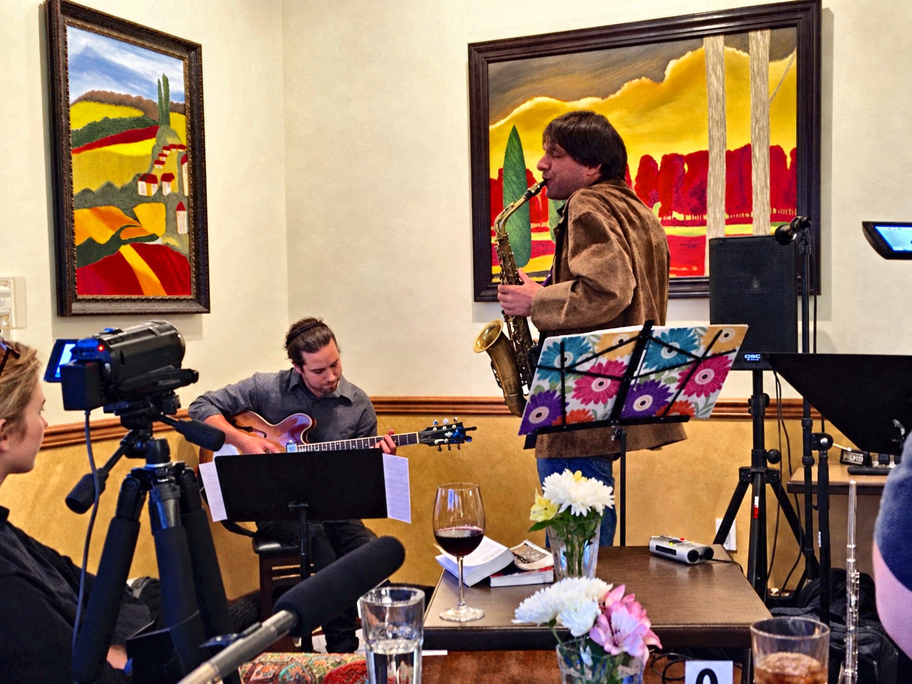 Dan Magay playing saxophone with a guitarist in a gallery, among paintings