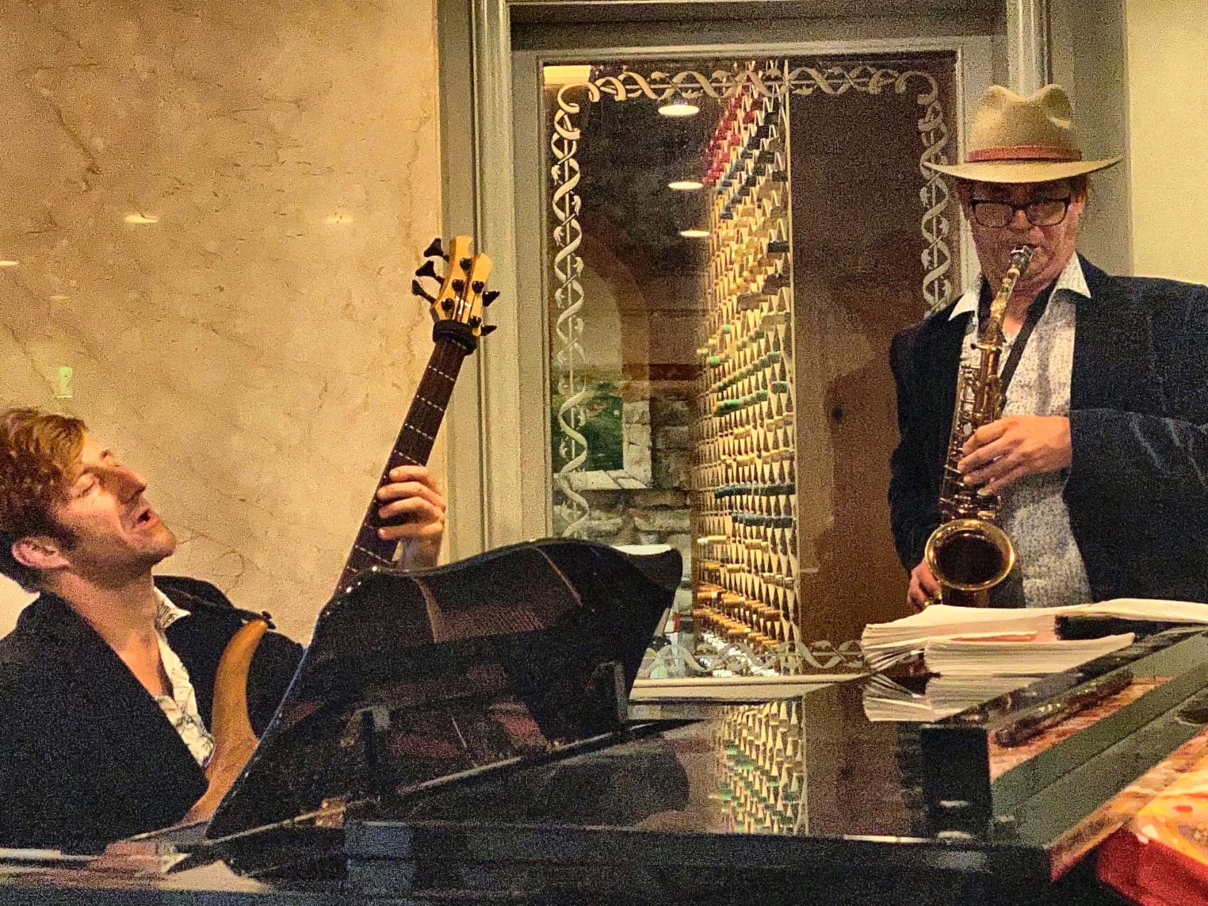 Dan in a hat, saxophone by the wine wall, pianist singing